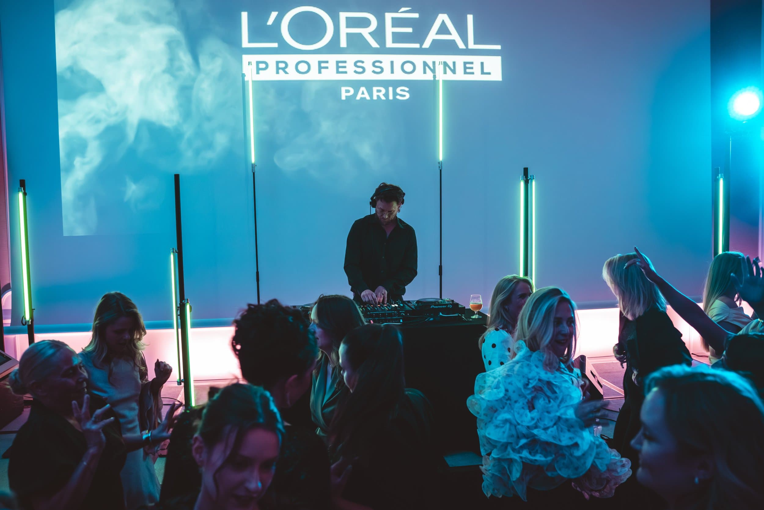 DJ i Trondheim i silhuett foran en projisert L'Oréal Professionnel-logo, med dansende gjester i forgrunnen