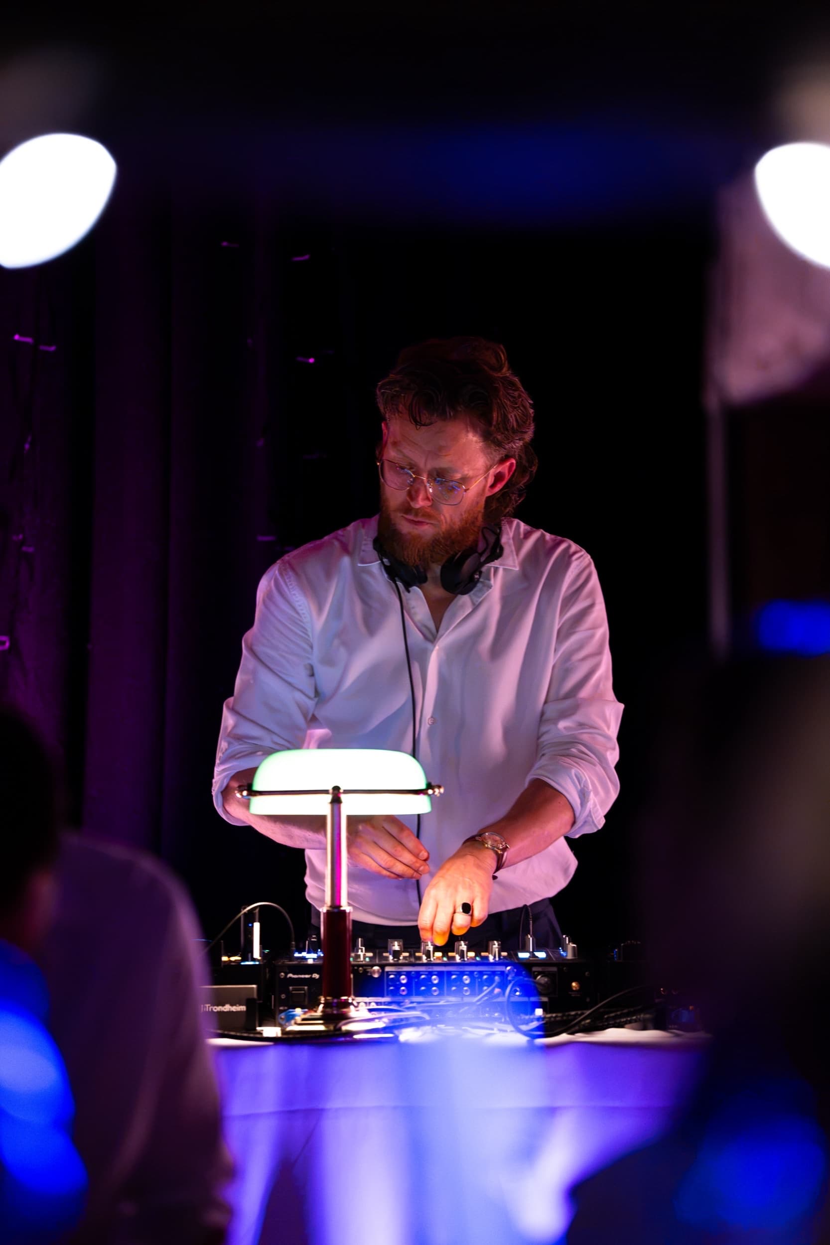 DJ i Trondheim justerer knapper på miksepulten, med selskapets branding synlig på utstyrskofferten