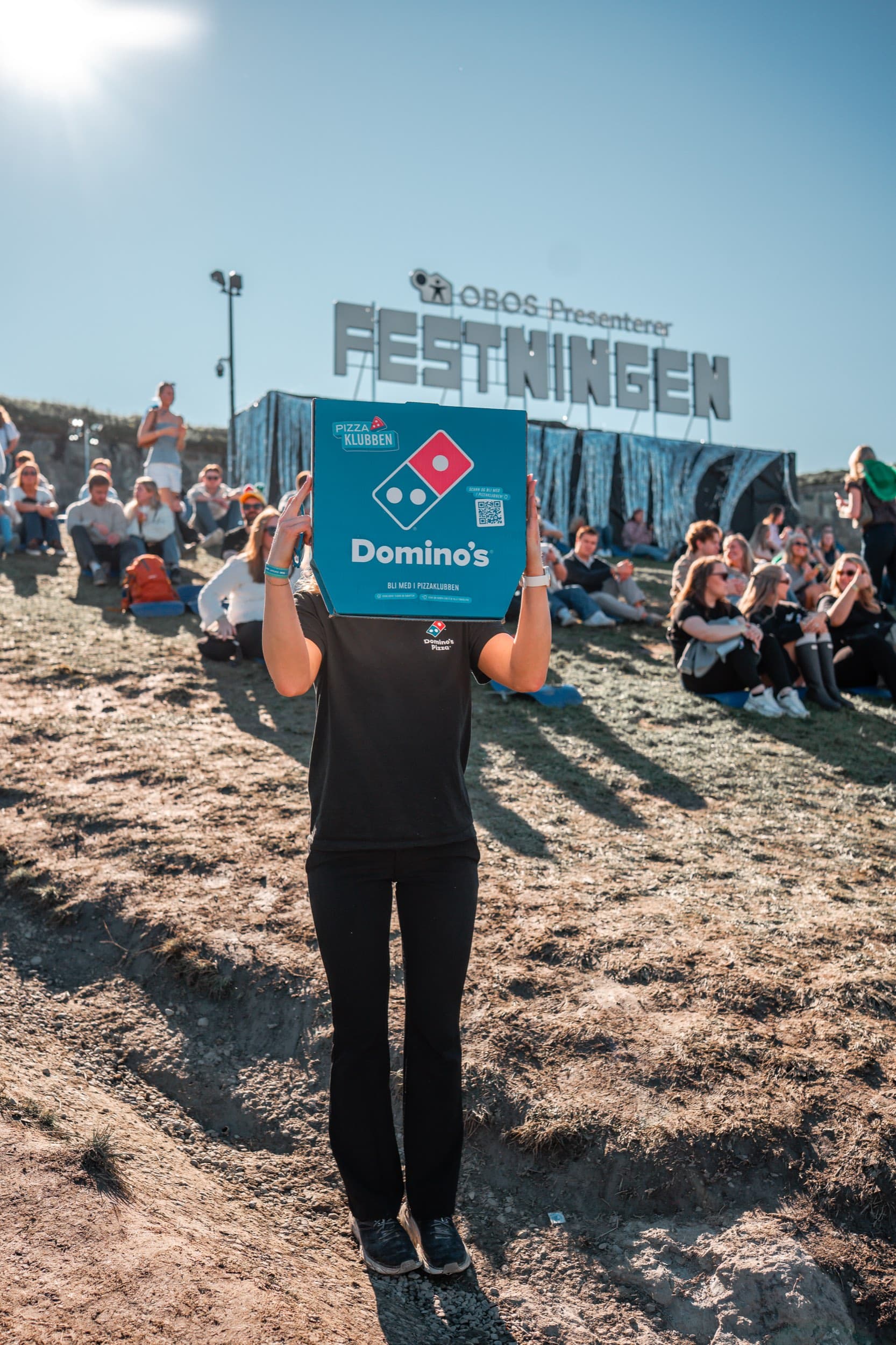 Domino's-ansatt sitter med en pizzaeske mellom to oppblåsbare enhjørninger