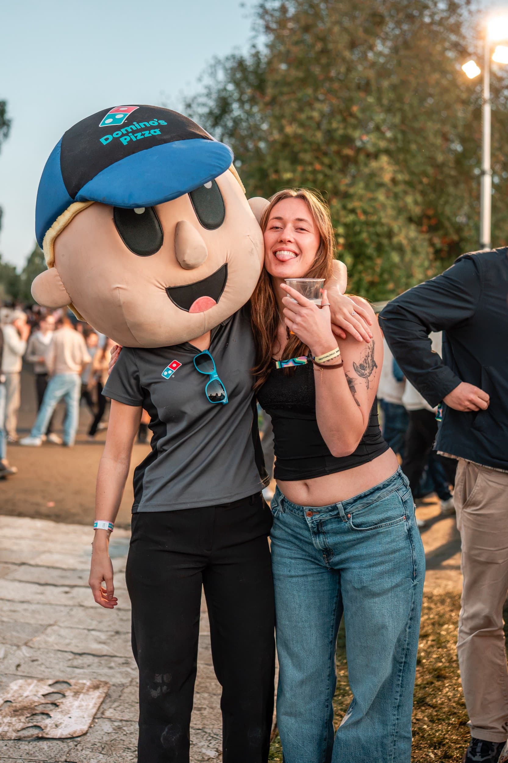 Domino's-maskoten og en festivalgjest smiler sammen foran vogna