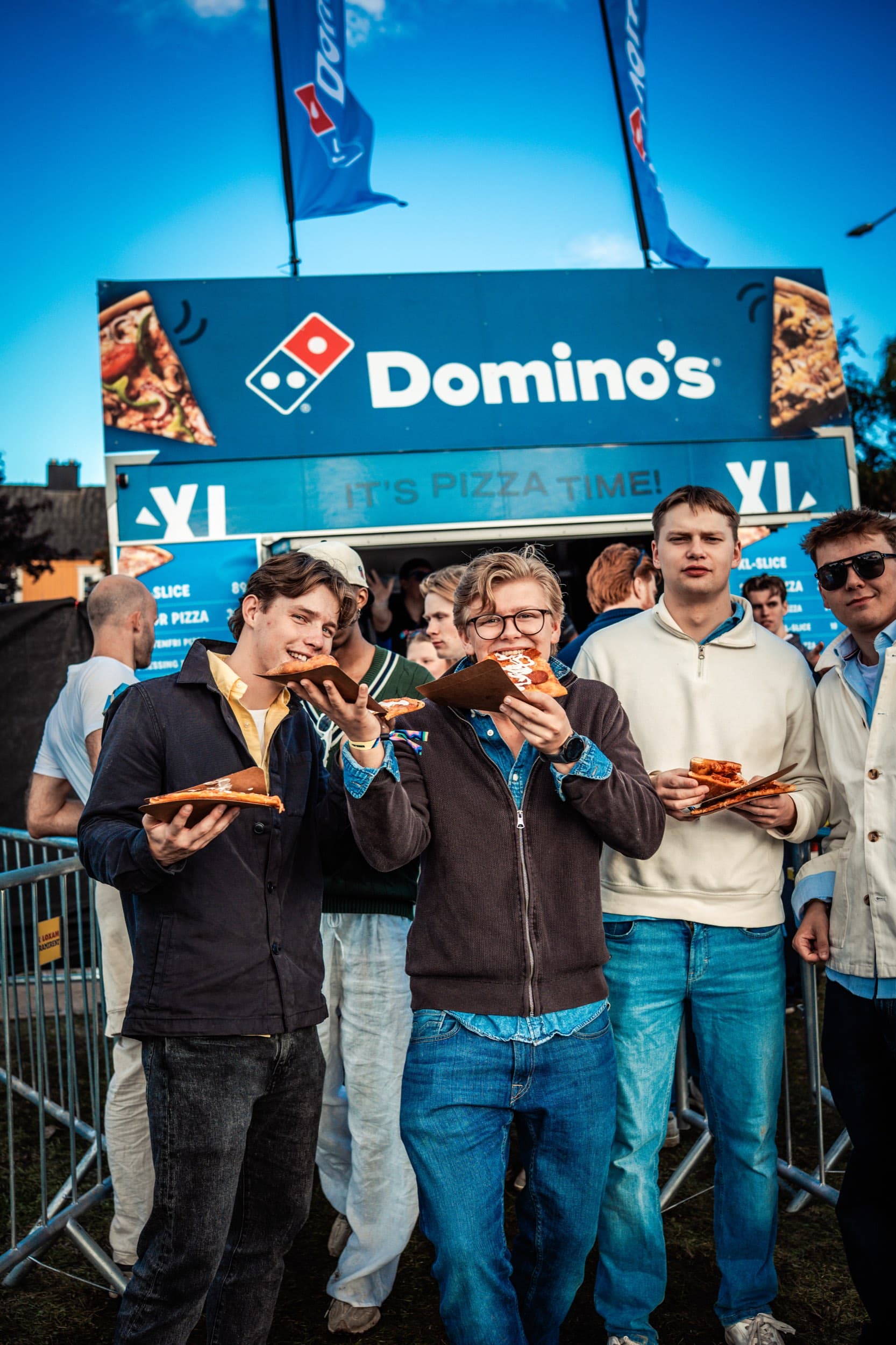 En vennegjeng spiser pizzaskiver foran Domino's-vogna i kveldslys