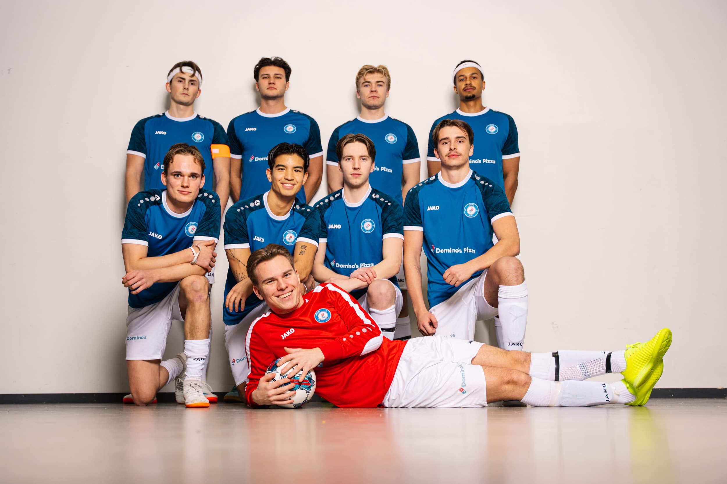 Lagbilde av Domino's Elite i blå drakter, med keeper i rødt liggende foran laget