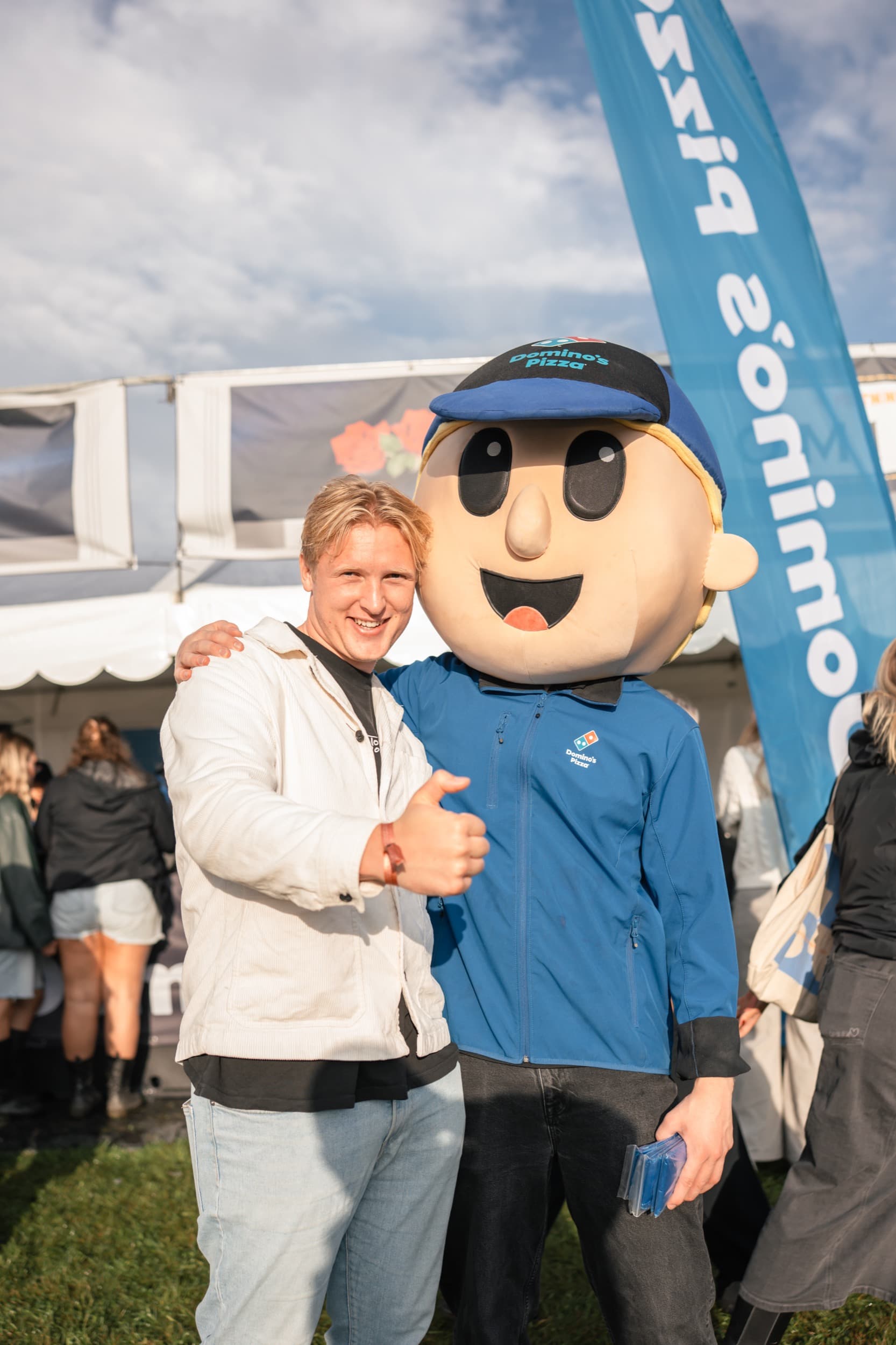 En festivalgjest gir tommel opp ved siden av Domino's-maskoten foran standen på Festningen.