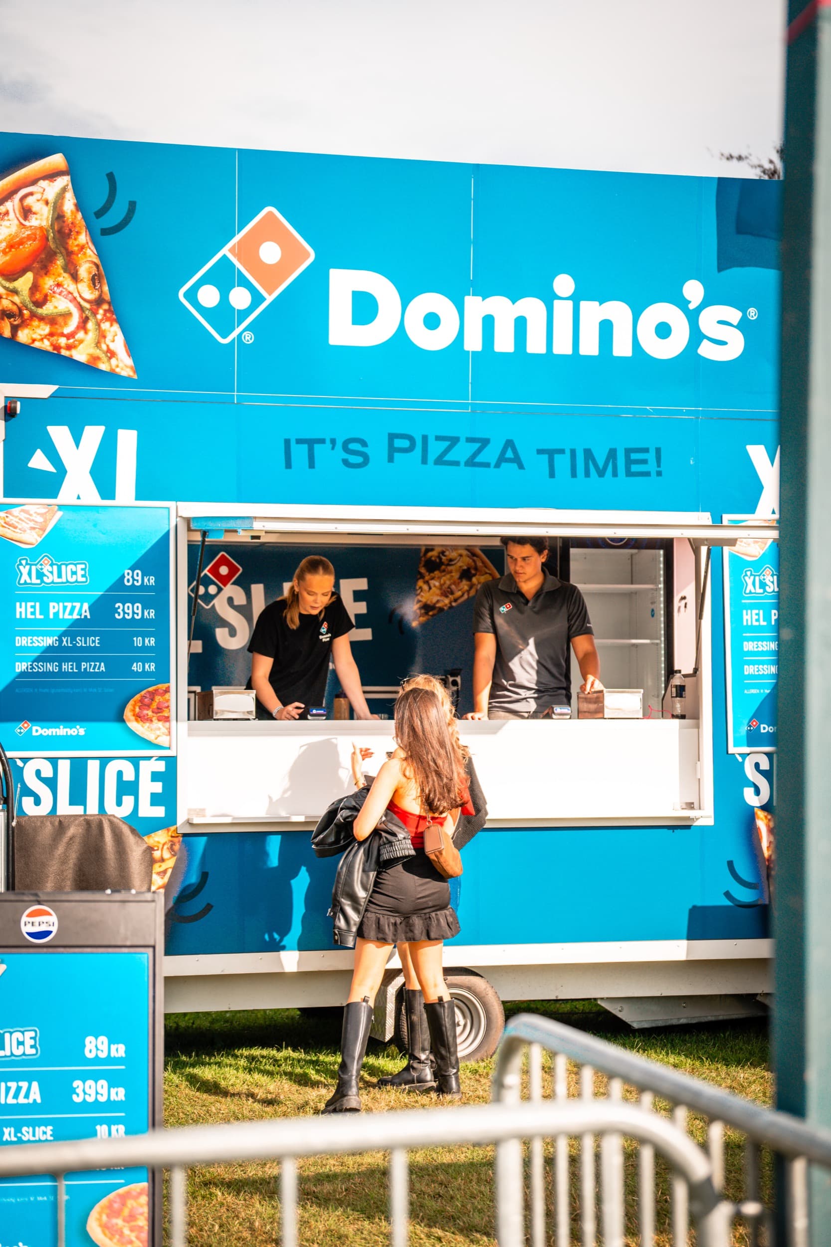 En gjest bestiller ved luken på Domino's sin matvogn, med to crew-medlemmer synlig innenfor