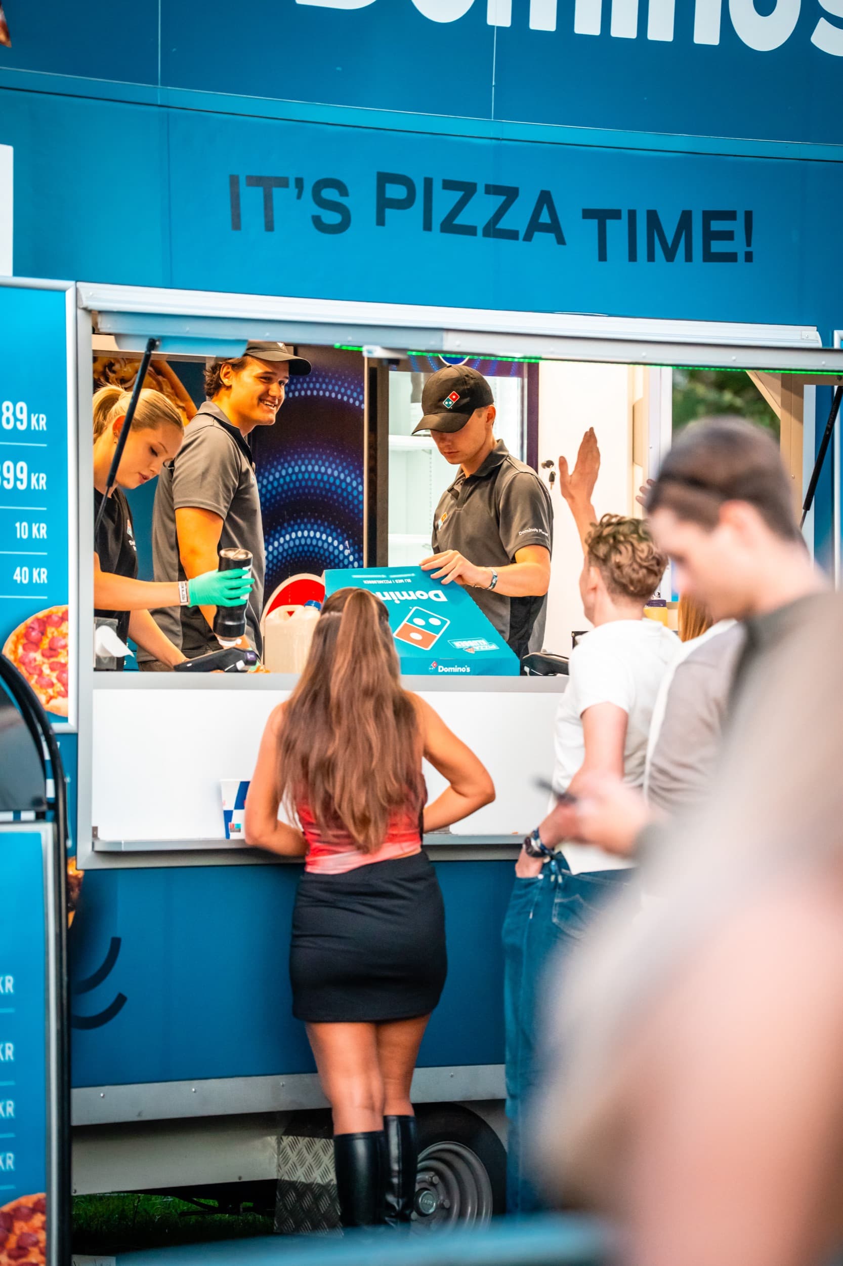 Domino's-crew rekker fram en pizzaeske til en gjest ved luken på matvogna