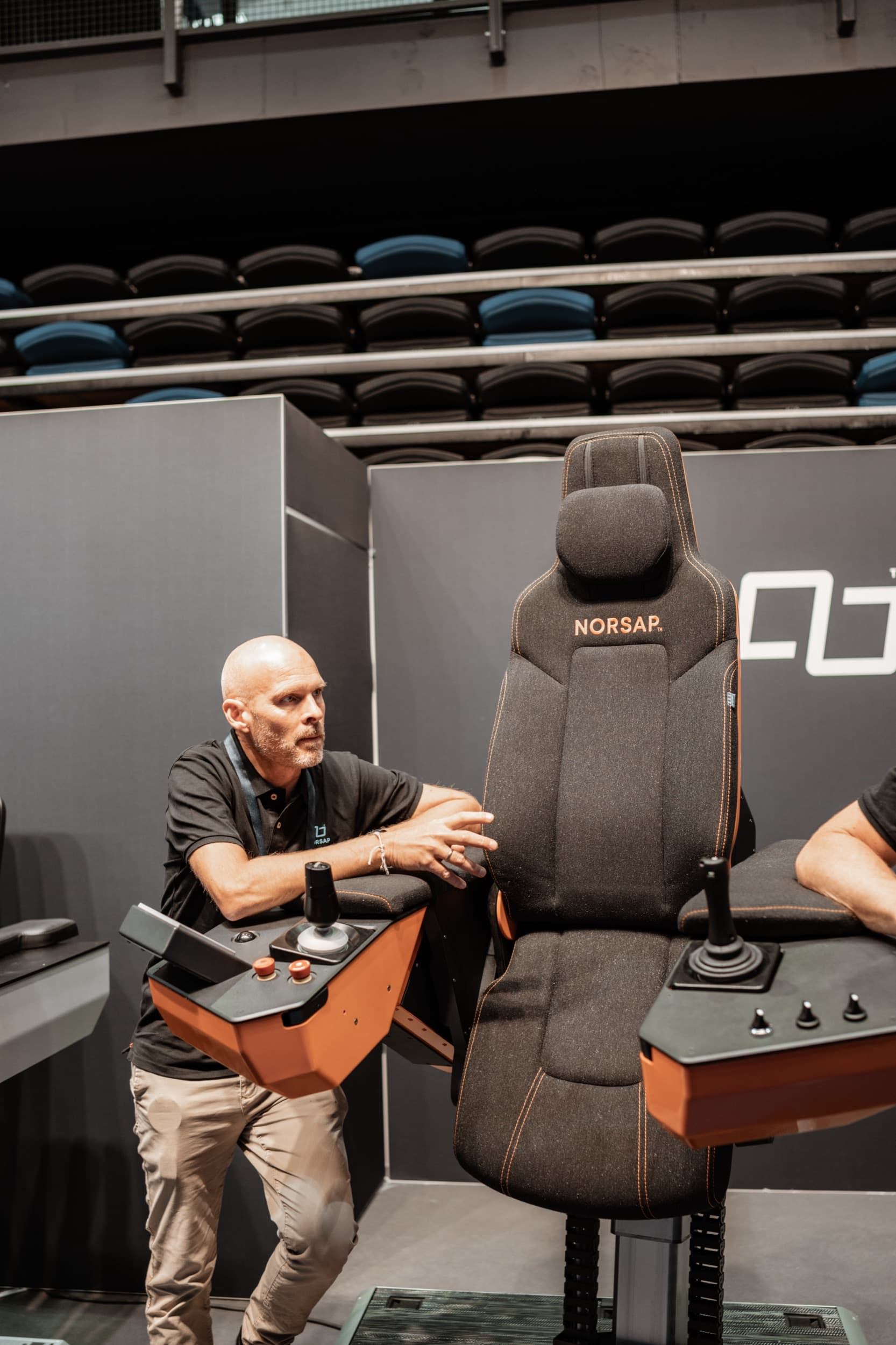 En mann demonstrerer en ergonomisk kontrollstol med joystick på en utstillerstand
