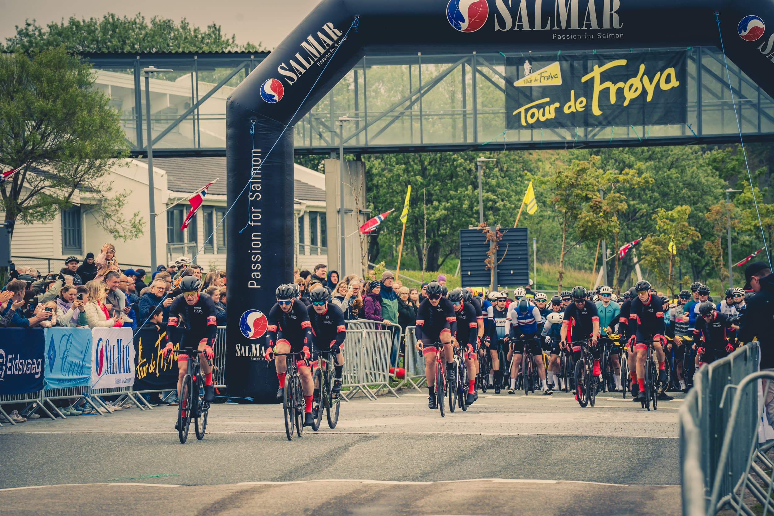 Ryttere starter Tour de Frøya under startbuen, med publikum langs løypa