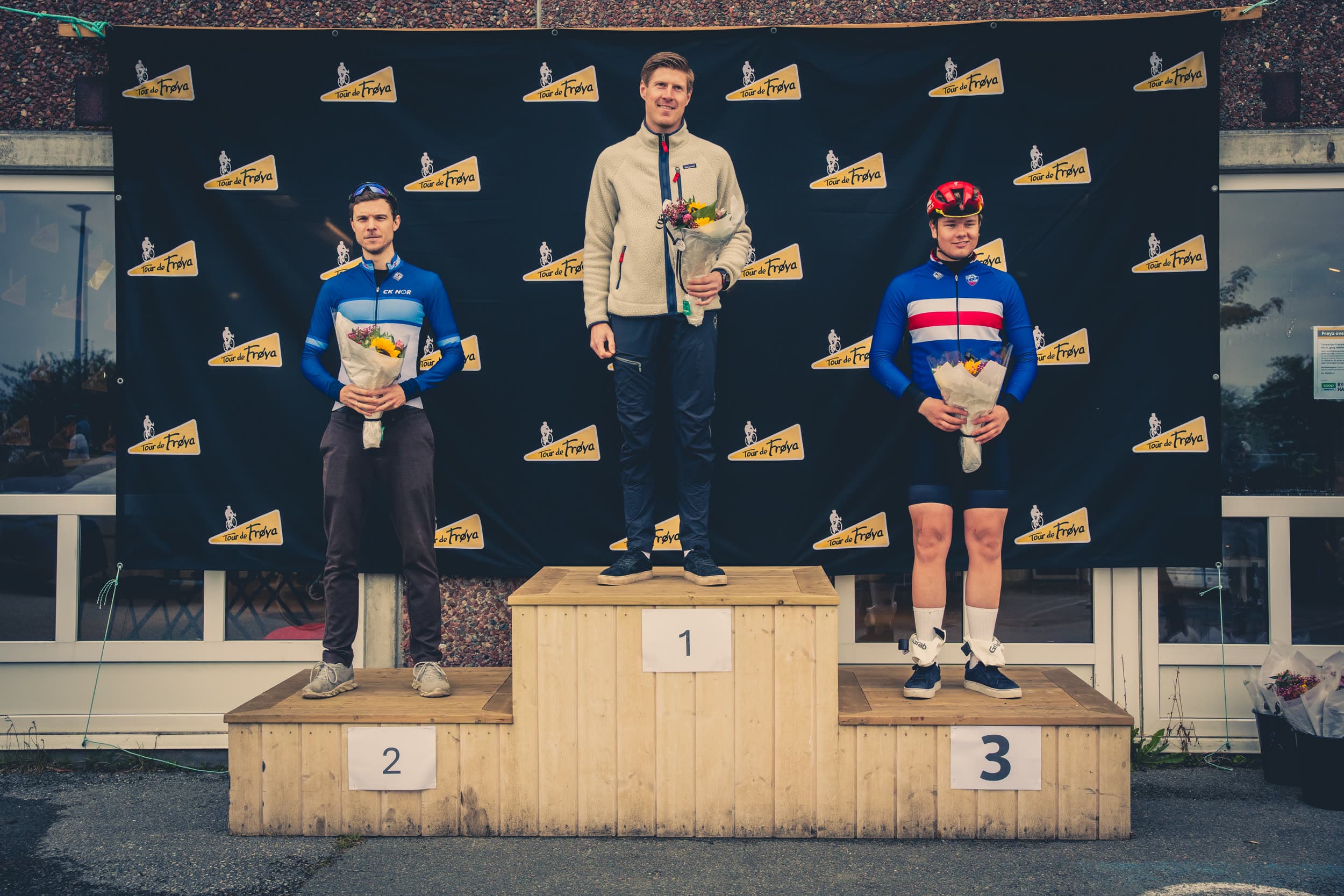 Tre ryttere på seierspallen under Tour de Frøya, med blomster og medaljer